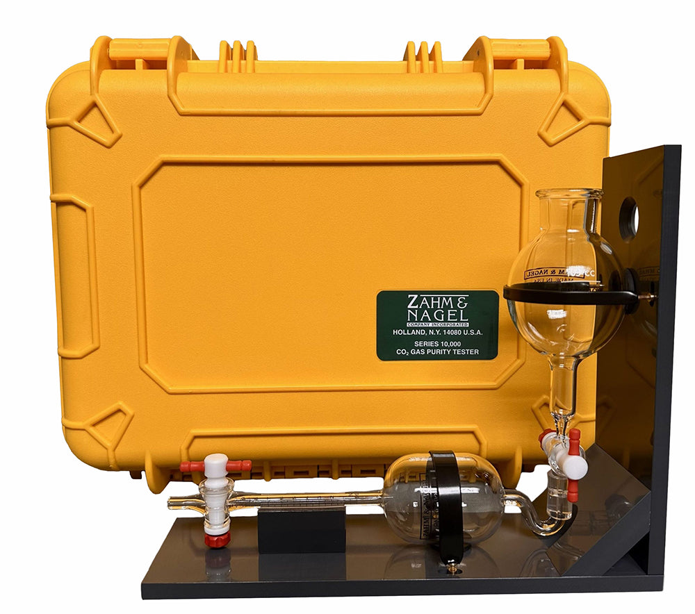 A yellow hard-shell carrying case with a black base and glass apparatus, branded with a green 'Zahm & Nagel' label. The setup includes a glass bulb, tubing, and a glass fractionating column on a black display stand against a white background.